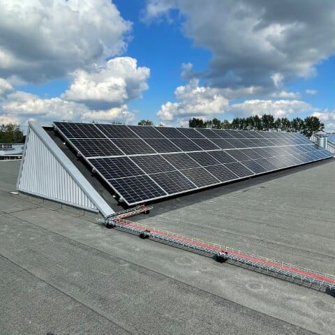 Zonnepanelen installatie op plat dak onder deels bewolkte lucht, duurzame energieopwekking met zonnepanelen, bomen op de achtergrond.