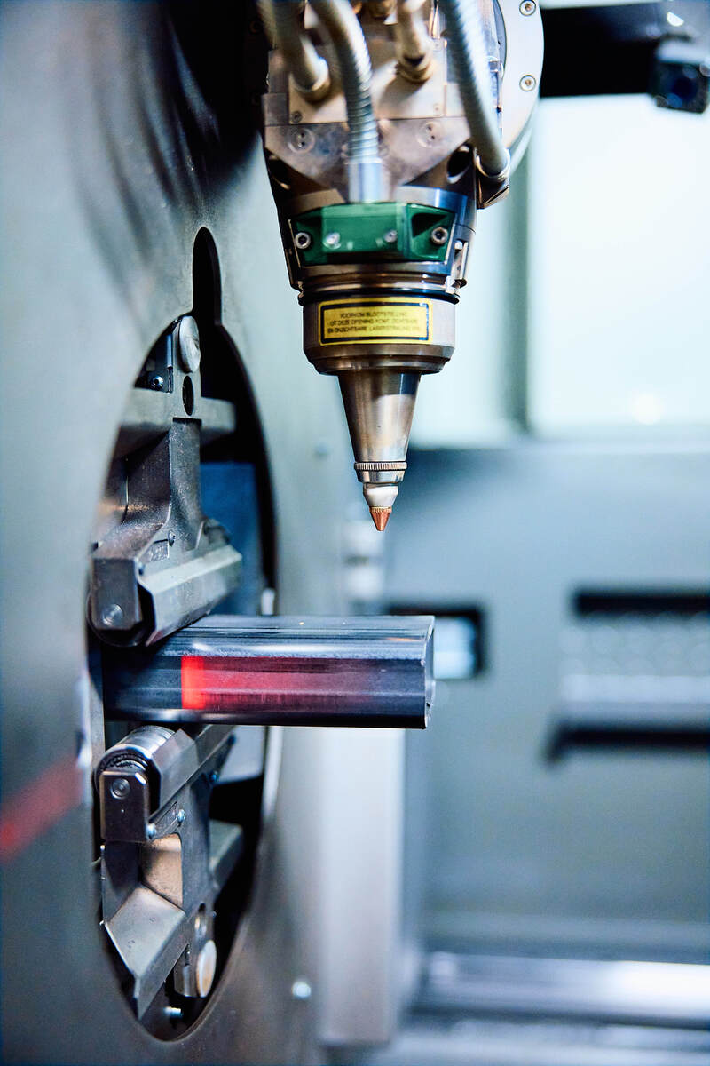 close-up van buislasersnijmachine die rechthoekig metalen werkstuk bewerkt met klemmen en laserunit