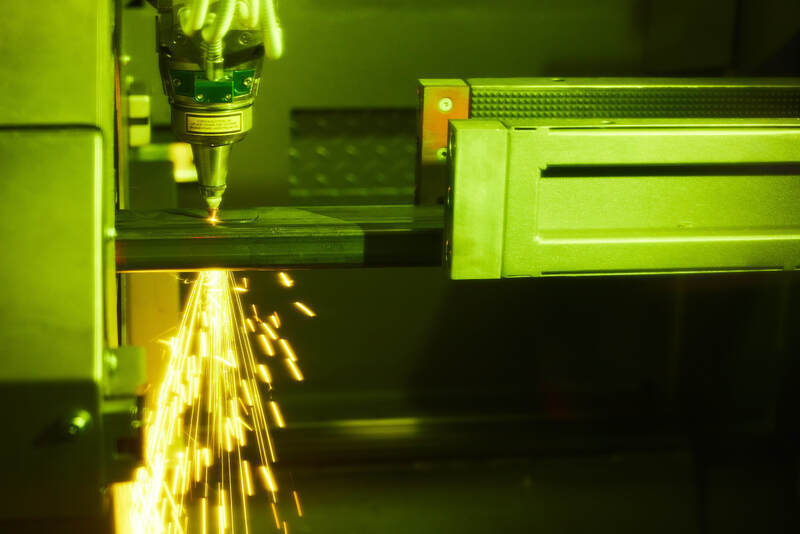 Close-up van buislasersnijmachine die metaal snijdt met vonken, onder groene industriële verlichting