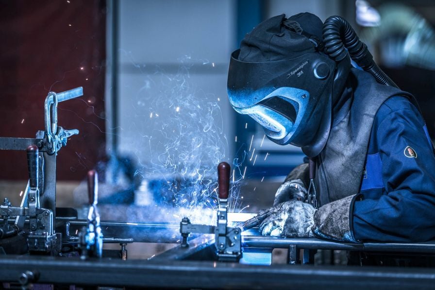 Metaalbewerking met lasser die nauwkeurig staal verbindt in moderne werkplaats met vonken en beschermende uitrusting.