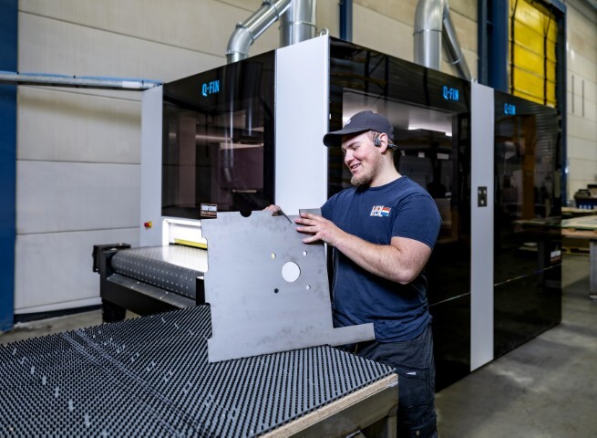 VDL-medewerker verwerkt een metalen plaat met uitsparingen naast een Q-FIN-machine, in een moderne productieomgeving ondersteund door OrderOn’s slimme orderverwerking.