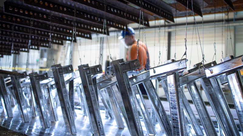 Hot-dip verzinken van metalen onderdelen in industriële faciliteit – metalen frames worden ondergedompeld in zinkbad onder toezicht van medewerker met beschermende uitrusting, voor corrosiebescherming en duurzaamheid.