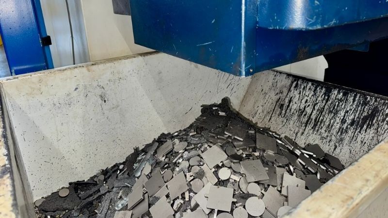 Container met metalen schroot onder een industriële CNC-machine, gevuld met glanzende, onregelmatige metaalstukken afkomstig van productie- of verspaningsprocessen.