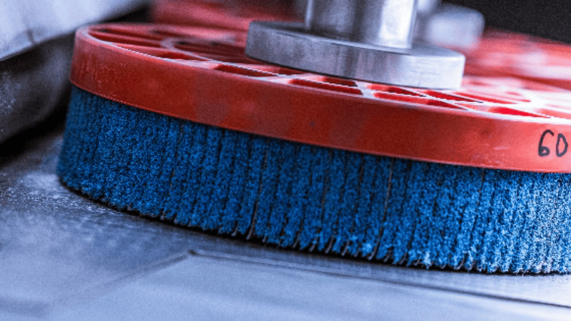 Industriële ontbraammachine , kantafronding met blauwe haren en rode kunststof basis gemonteerd op roterende as – geschikt voor mechanisch reinigen, polijsten en oppervlaktebehandeling in productieomgevingen.
