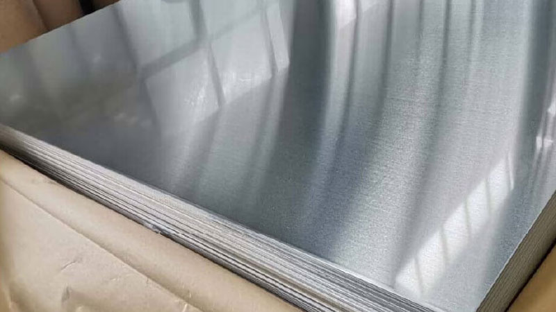 Stapel metalen platen met glad, reflecterend oppervlak in een kartonnen doos, mogelijk aluminium of staal.